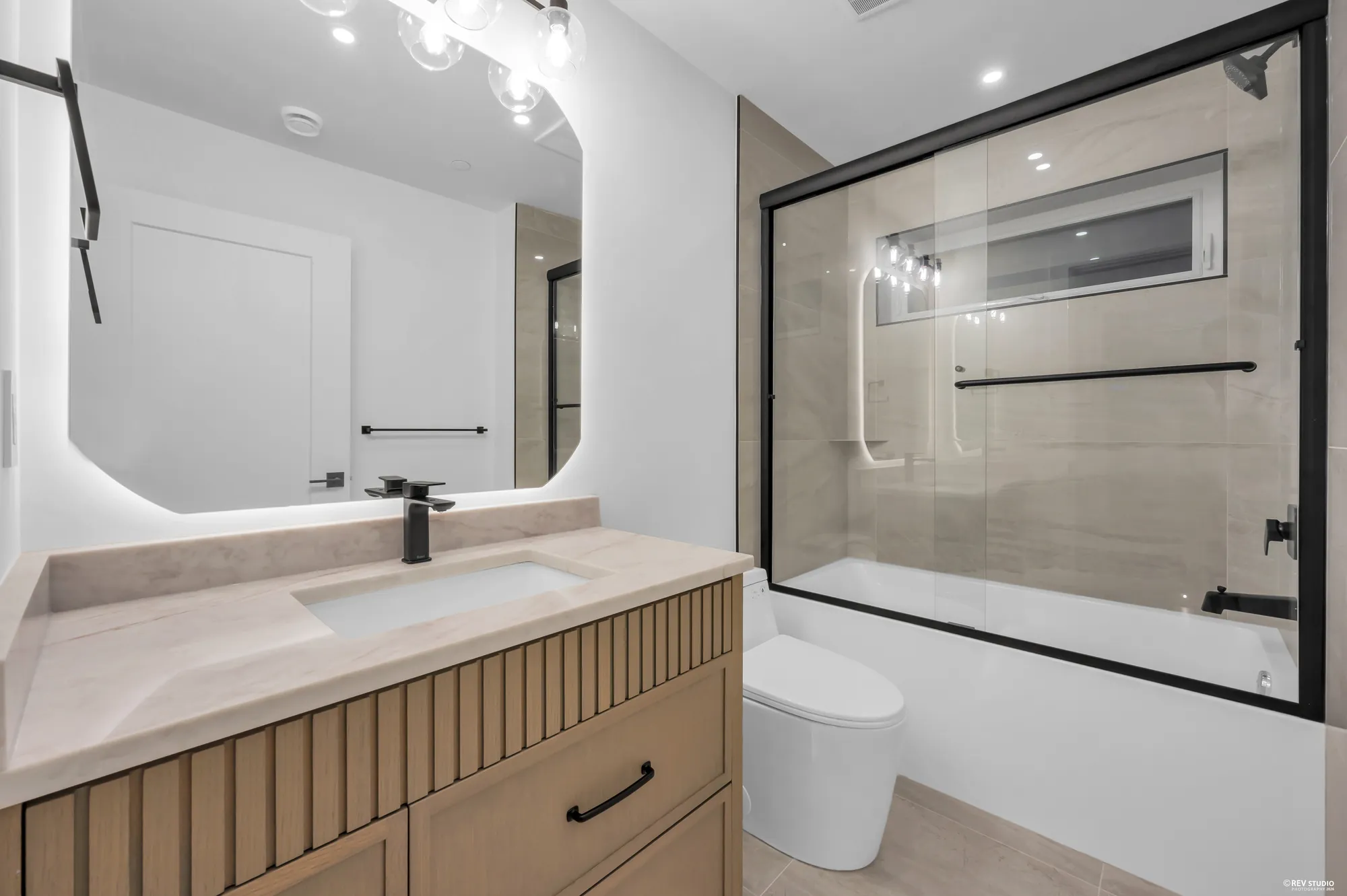 Bathroom with a tub behind a glass screen and a fluted vanity