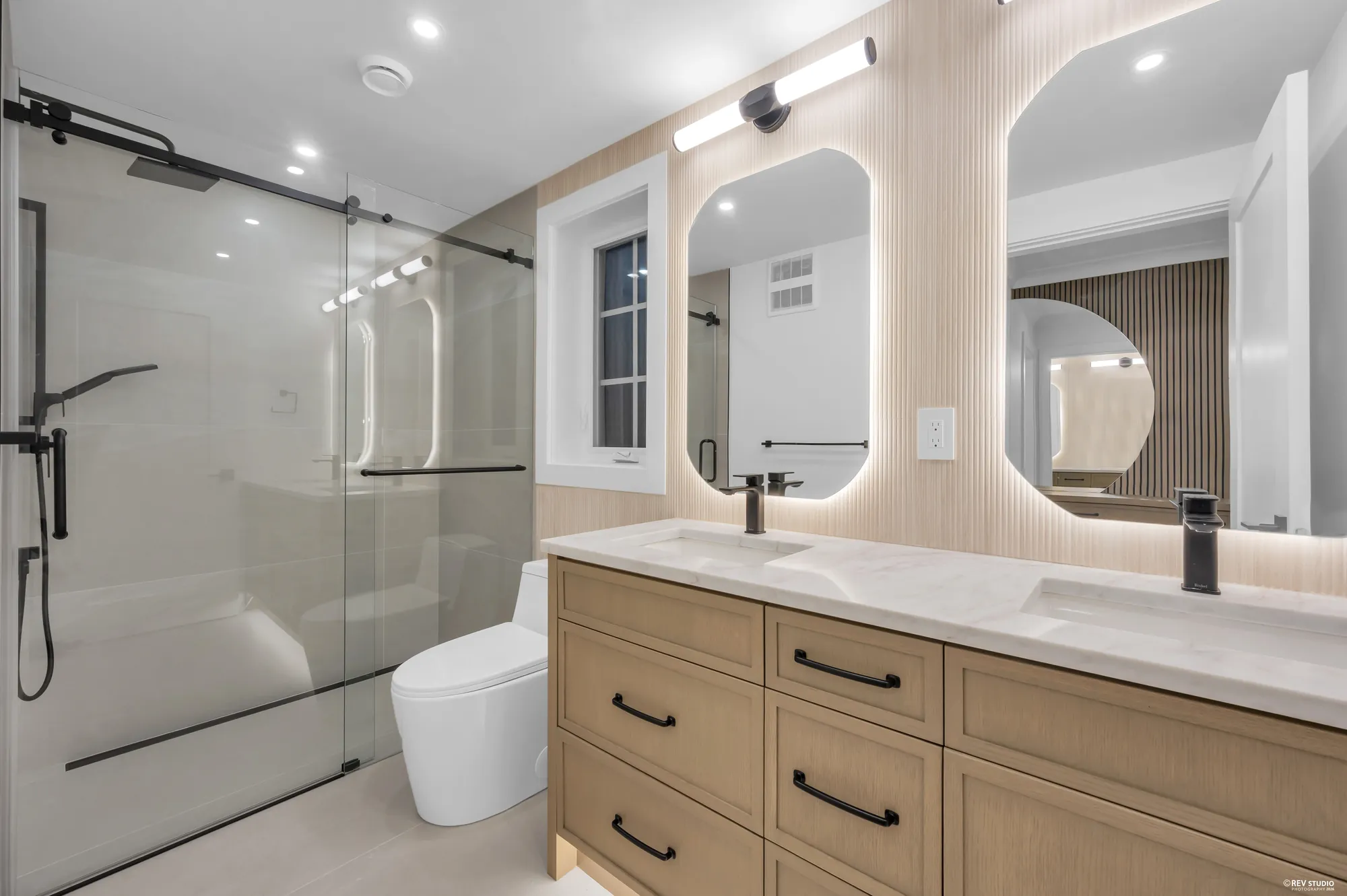 Bathroom with a double vanity, glass shower and backlit mirrors