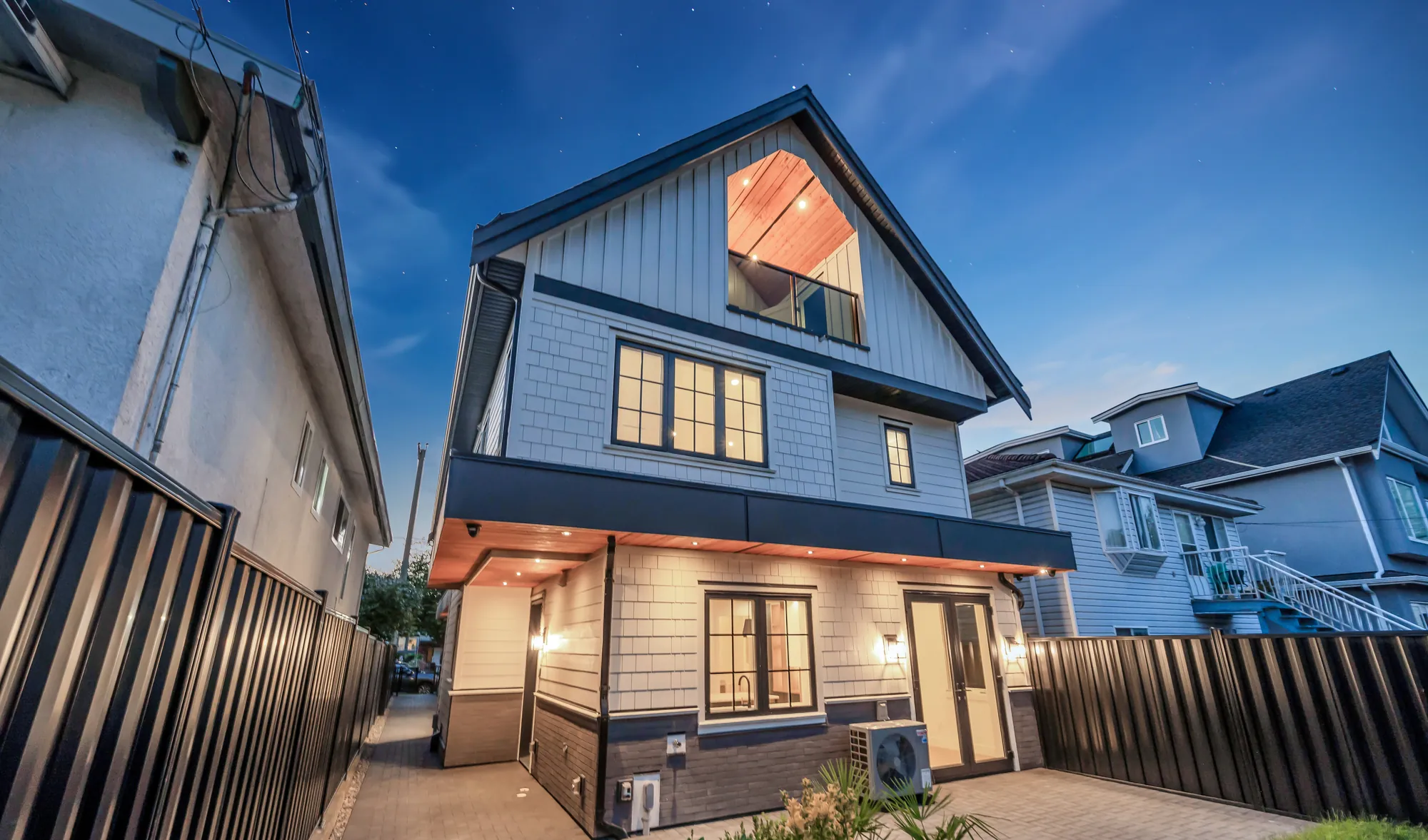 2-5150 Spencer Street at dusk: a new board-and-batten house with dark trim, its windows lit from inside